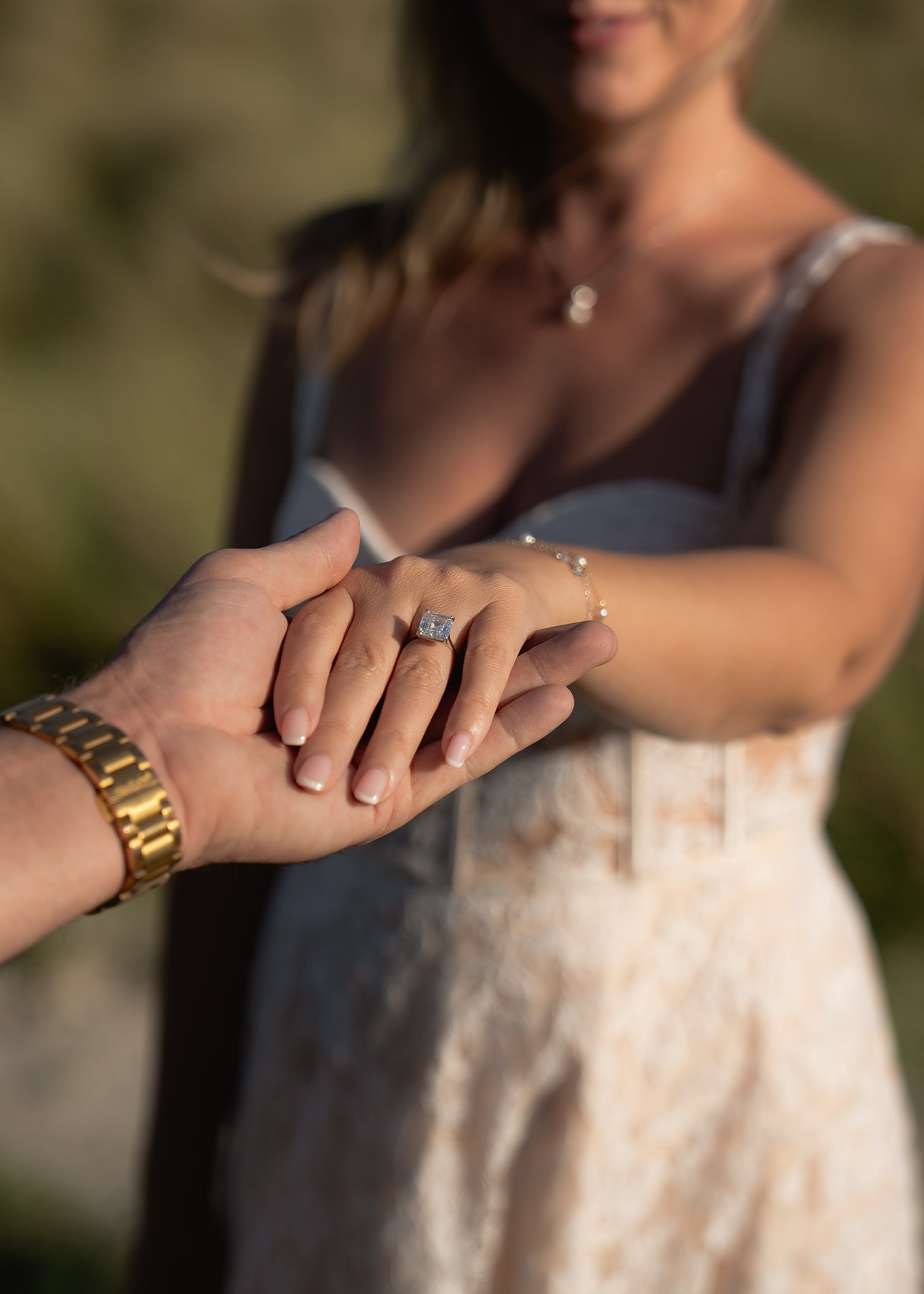 Engagement ring close-up on woman’s hand held by her partner, captured in soft natural light outdoors.