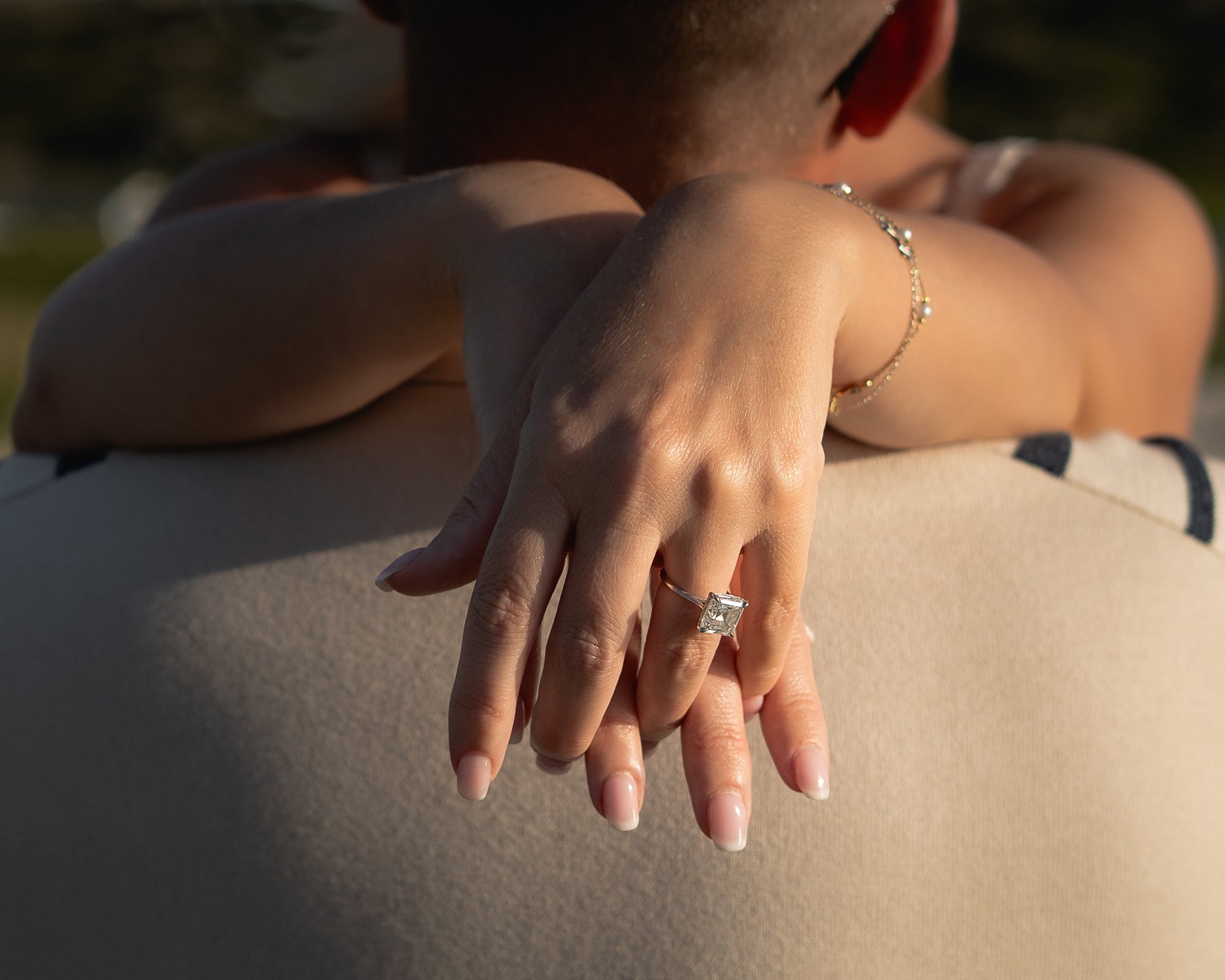 Close-up of a woman's hand resting on her partner's shoulder, showing a sparkling engagement ring.