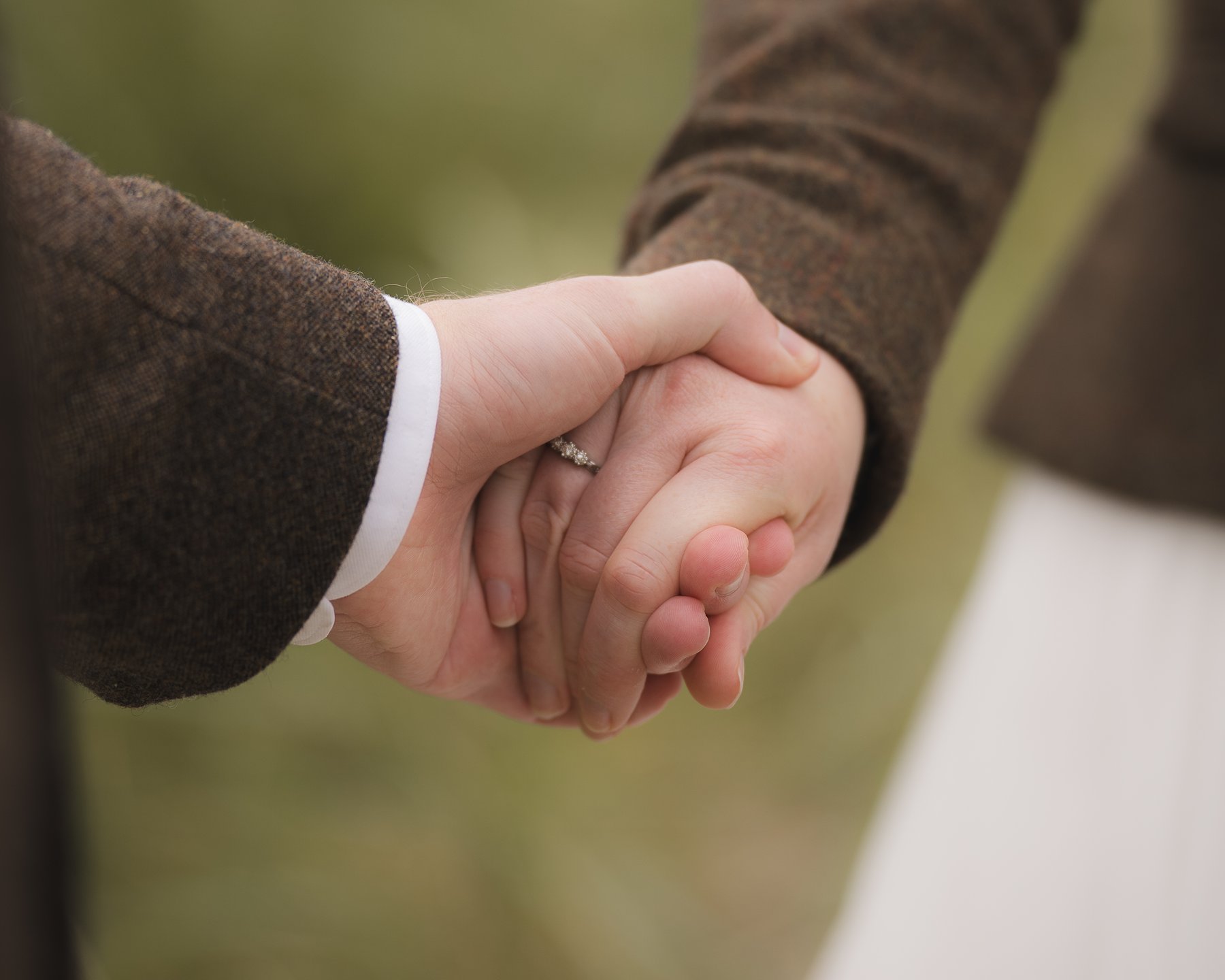 Close-up of a holding hands, with a wedding ring visible on the bride’s finger.