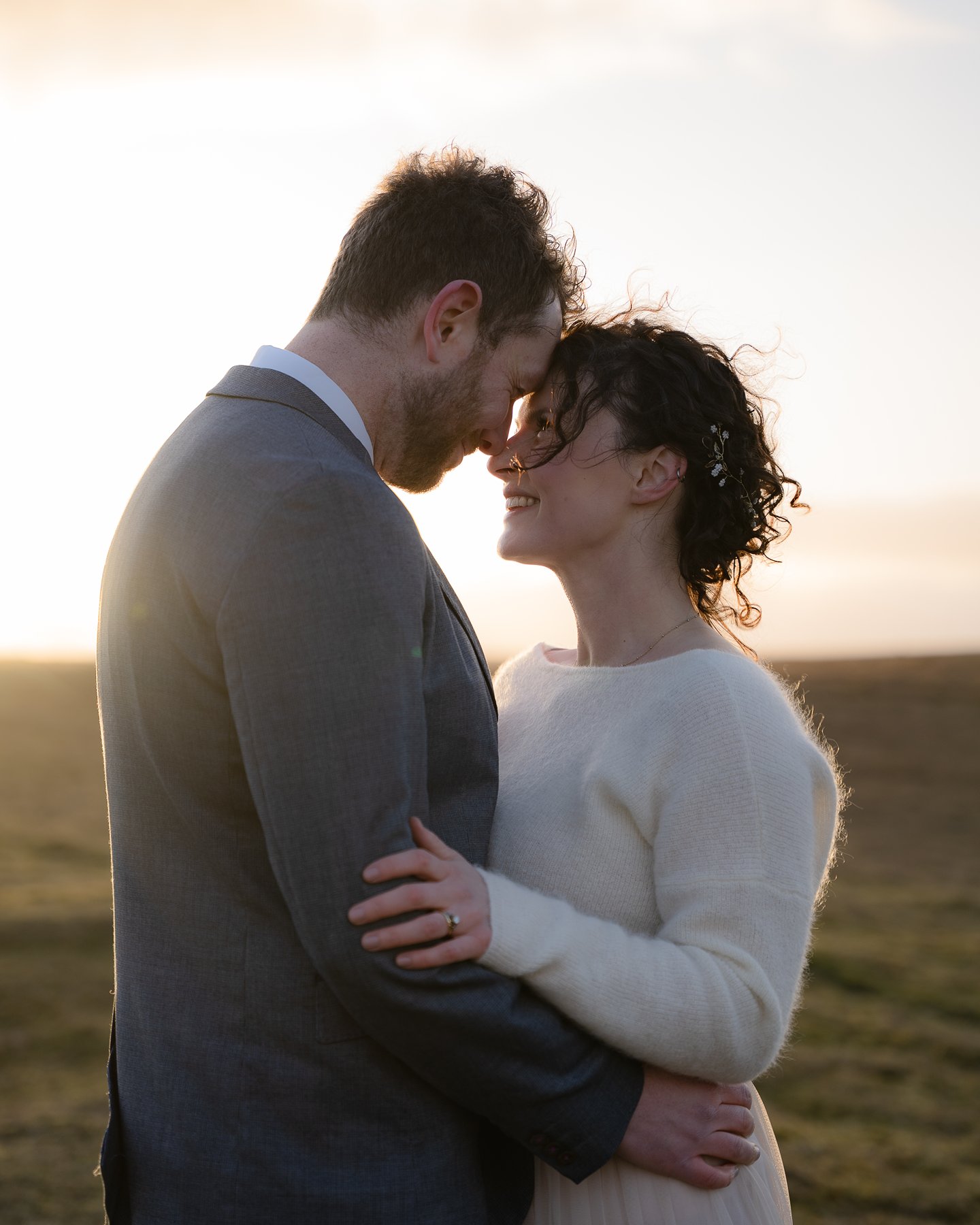 Couple embrace at sunset, touching foreheads and smiling lovingly in an open field.