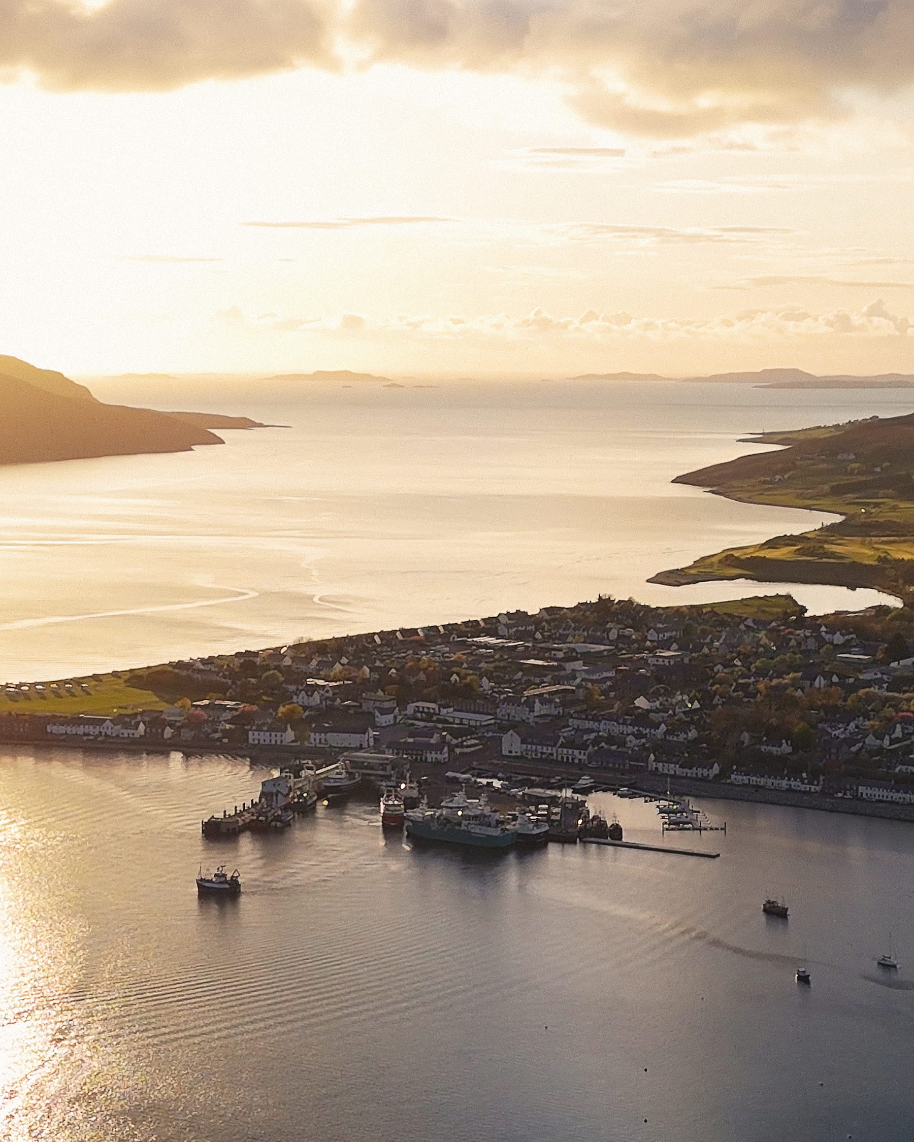 Aerial view of Ullapool village in the Scottish Hihglands with sun setting behind sea sea horizon.